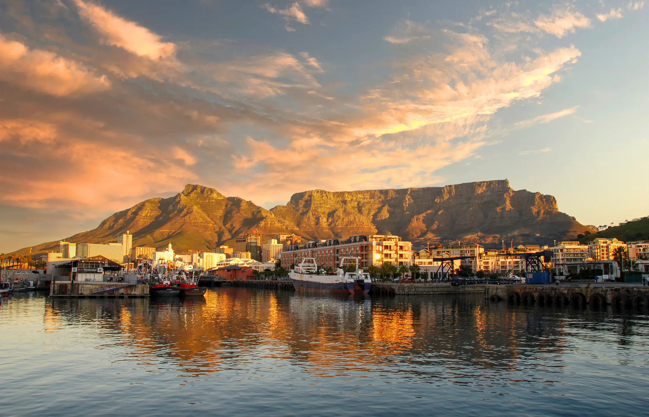Cape Town’s V&A Waterfront at golden hour with boats docked and Table Mountain in the background, South Africa